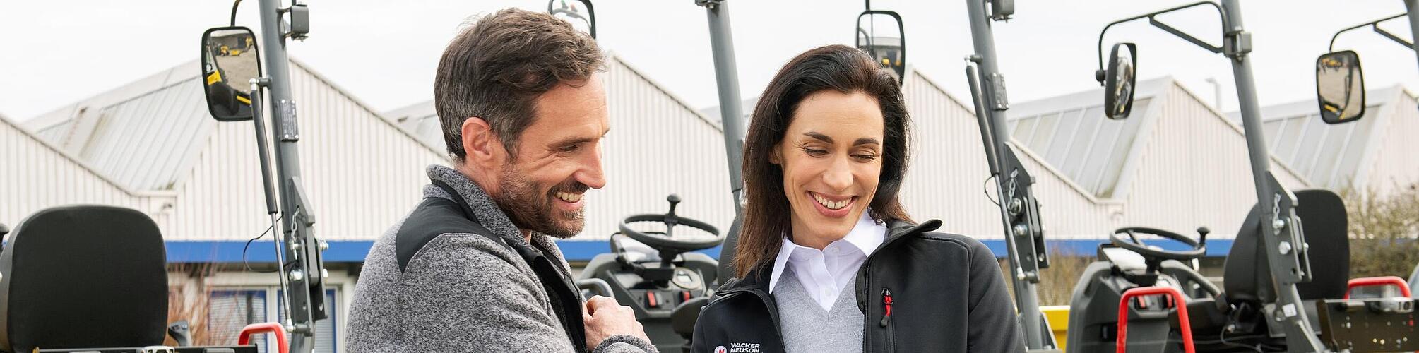 威克诺森员工面带微笑，使用平板电脑在威克诺森建筑机械前为微笑着的客户提供建议。